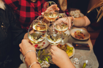 Close up shot of group of people clinking glasses with wine or champagne in front of bokeh...