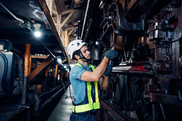 Male engineer maintenance locomotive engine wearing safety uniform, helmet and gloves work in locomotive repair garage. 