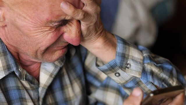 annoyed pensioner holding a smartphone and experiencing the loss of money from phone scammers, having learned the good news of the loss