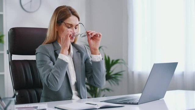 Taking off the glasses, tired. Woman in business formal clothes is working in office.