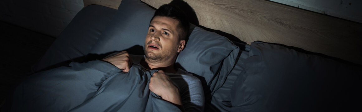 top view of scared man suffering from panic attacks and having insomnia while lying under blanket, banner.