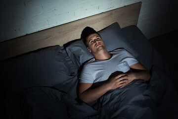 top view of awaken young man with ptsd lying on bed and having insomnia at night.