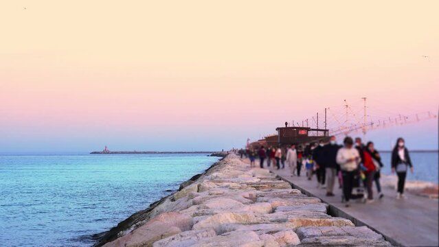 People in masks with children walk on rocky pier at sunset
