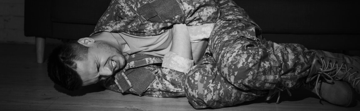 black and while photo of anxious serviceman suffering from post traumatic stress disorder while lying on floor, banner.
