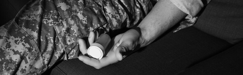 monochrome photo of military man in camouflage holding antidepressants at home, banner.
