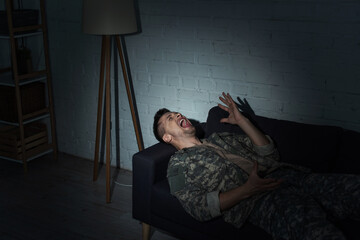 Fototapeta premium Irritated military man with post traumatic stress disorder screaming at home at night.