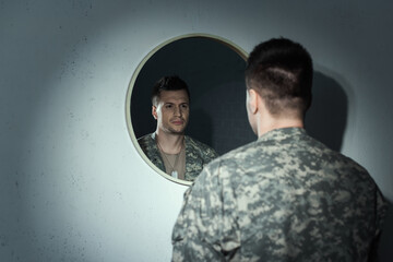 Blurred military veteran with emotional distress looking at mirror at home.