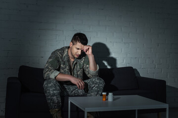 Frustrated military veteran with ptsd looking at pills on table at night time.