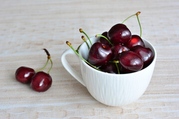 A white cup of dark cherries isolated on a table, close-up