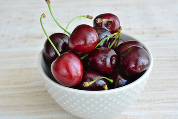 A bowl of cherries on a light wooden table isolated, macro 