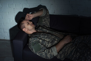 Obraz premium Depressed military man in uniform suffering from post traumatic stress disorder while lying on couch.