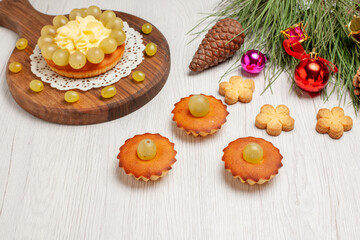 front view cream cake with little sweet cakes and grapes on white desk fruit cookie cake biscuit pie