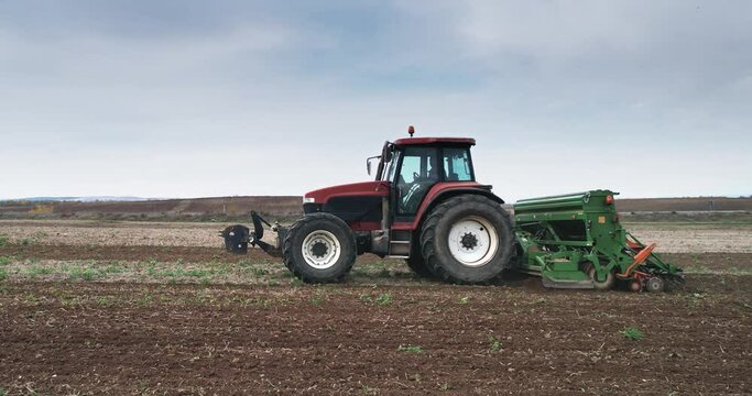 Spring agricultural field work, a tractor with a mounted seeder sow seeds in the ground on an field. aerial video