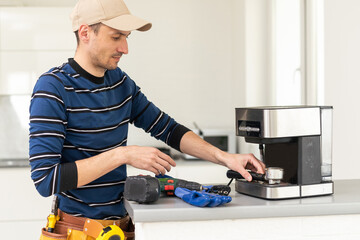 Professional young repairman repairs a coffee maker. Handsome worker in uniform repairing coffee machine in a workshop.