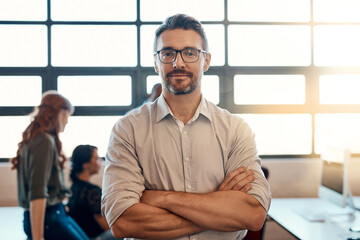 He knows how to get a team to get results. Portrait of a confident mature businessman standing in a modern office with his colleagues in the background. - obrazy, fototapety, plakaty