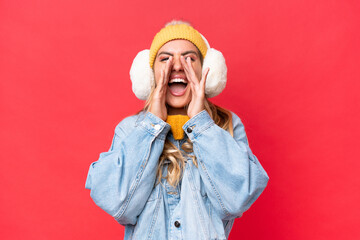 Young pretty Uruguayan woman wearing winter muffs isolated on red background background shouting...