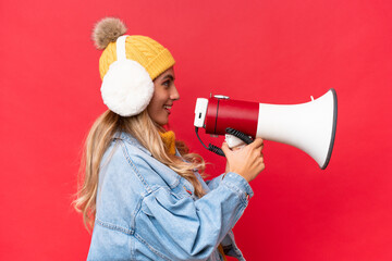 Young pretty Uruguayan woman wearing winter muffs isolated on red background background shouting through a megaphone