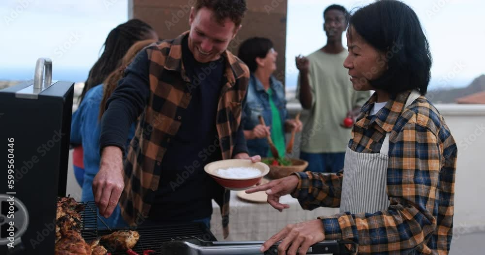 Wall mural Multi generational people doing barbecue during weekend day at home's rooftop preparing food - Multiracial friends having fun together - Asian woman cooking chili and chicken on bbq grill