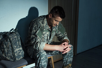 Military man in uniform suffering from post traumatic stress disorder while sitting in hallway at home.