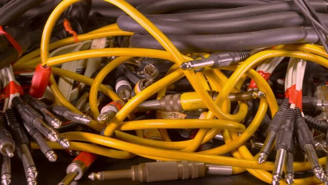 Closeup pan shot of an untidy pile of professional audio studio, analog wiring looms of jack and phono plugs, for traditional analog multitrack recording.