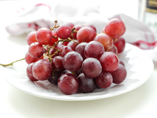 Fresh red grapes fruit in white plate on white background
