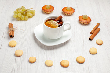 front view little yummy cakes with grapes cup of tea and cookies on white desk fruit cake biscuit sweet dessert tea