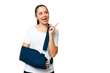 Young blonde woman with broken arm and wearing a sling over isolated chroma key background intending to realizes the solution while lifting a finger up