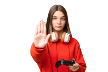 Teenager caucasian girl playing with a video game controller over isolated background making stop gesture
