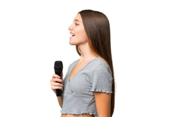 Teenager singer girl picking up a microphone over isolated background laughing in lateral position