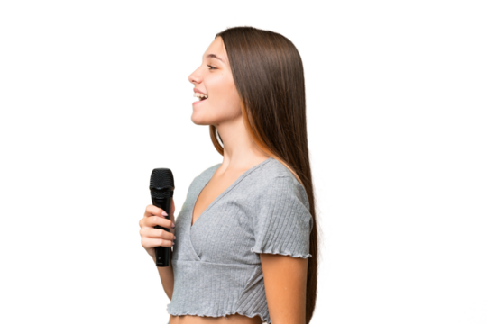 Teenager singer girl picking up a microphone over isolated background laughing in lateral position - Powered by Adobe
