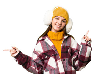 Teenager caucasian girl wearing winter muffs over isolated background pointing finger to the laterals and happy