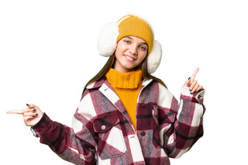 Teenager caucasian girl wearing winter muffs over isolated background pointing finger to the laterals and happy