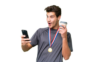 Young caucasian man with medals over isolated background holding coffee to take away and a mobile