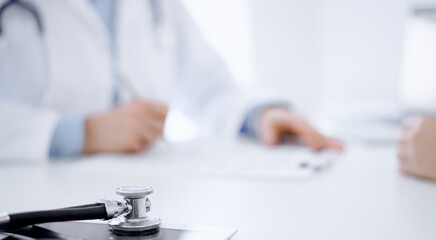 Fototapeta premium Stethoscope lying on the tablet computer in front of a doctor and patient sitting opposite each other at the background . Medicine, healthcare concept