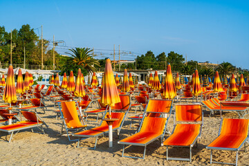 a row of sun loungers and umbrellas on an italian beach at sunrise against a railway and blue sky, panoramic background, premium photography, beach setting, authentic sustainability in one with nature - obrazy, fototapety, plakaty
