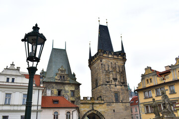 Fototapeta premium View of an antique buildings with colorful walls and medieval towers with blue top, street lantern and old sculpture. Charles Bridge. Prague, Czech Republic, October 2022.
