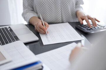Woman accountant using a calculator and laptop computer while counting taxes for a client. Business...