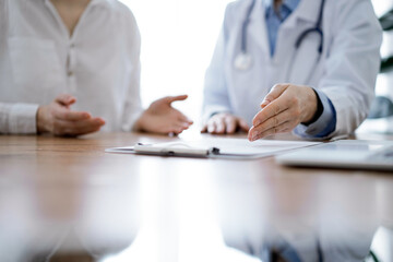 Fototapeta premium Doctor and patient discussing something while sitting near each other at the wooden desk in clinic. Medicine concept