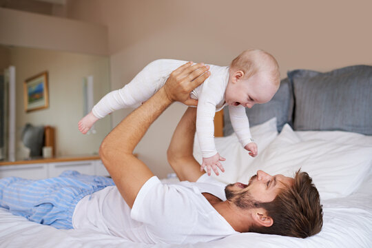 Father, On Bed And Holding His Baby Girl Up In The Air Or Playful Daughter And Having Fun In The Bedroom Feeling Happy. Parent, Kid And Dad Bonding Or Carefree And Excited Together In The House