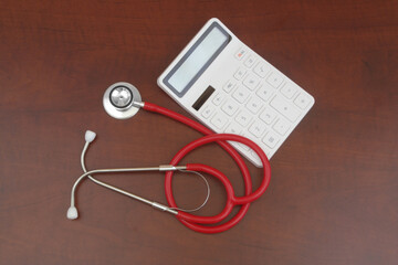 Red stethoscope and calculator on wooden table