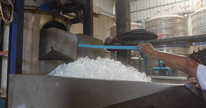 worker using a small rigid pipe to remove cube ice stuck into the ice machine 