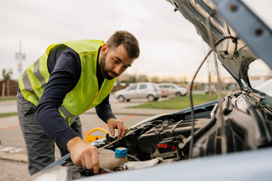 A Man is standing next to his car formally dressed and looking worried about the cars engine problem.