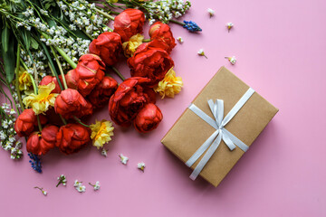 Fresh spring flowers and a gift box on color background, top view with space for text