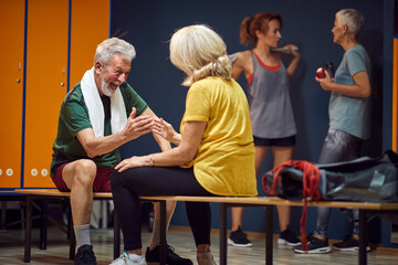 Mature man and woman in gym locker room, sitting facing each other and high fiving, feeling energized and ready for workout.