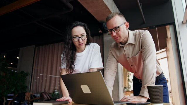 Task and problem solving in the office work. Male and female employees stand over the desk looking on the laptop. Low angle view.