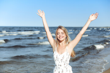 Happy blonde woman wearing sun glasses and relaxing on a wooden deck chair at the ocean beach