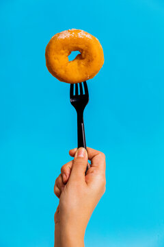 Crop unrecognizable person showing donut on fork in studio