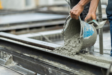 A male worker in a precast wall manufacturing factory (Precast) is pouring cement in a prepared mold to form a wall. - obrazy, fototapety, plakaty