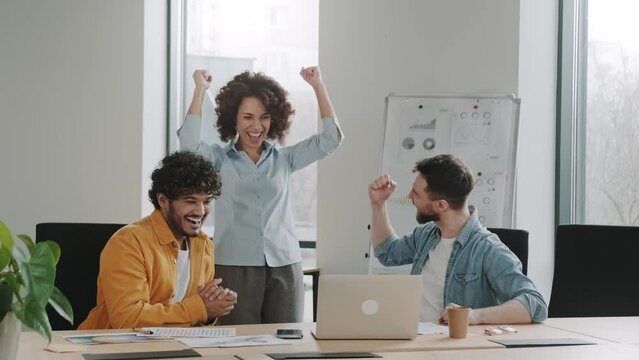 Multiracial euphoric business team people give high five at office table with laptop, happy excited diverse work group engaged in teambuilding celebrate corporate success win partnership power