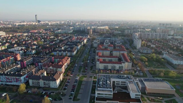An aerial shot taken by a drone, soaring over houses in a residential area during early morning in a city. A plethora of greenery amidst the houses